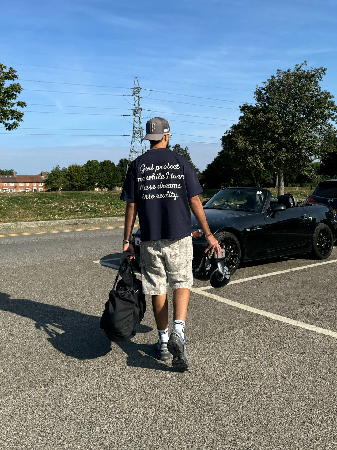 Person walking with a backpack and boxing gloves in a parking lot with cars and trees in the background 