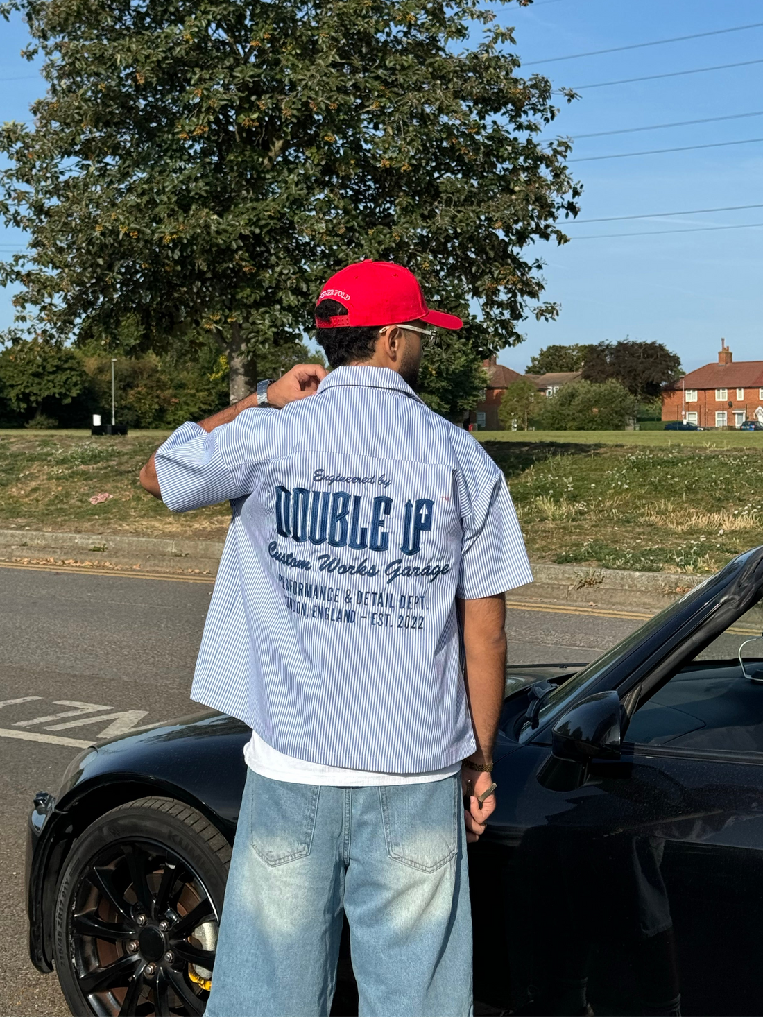 Person wearing a light blue jacket with 'DOUBLE UP' branding, standing next to a black car outdoors.