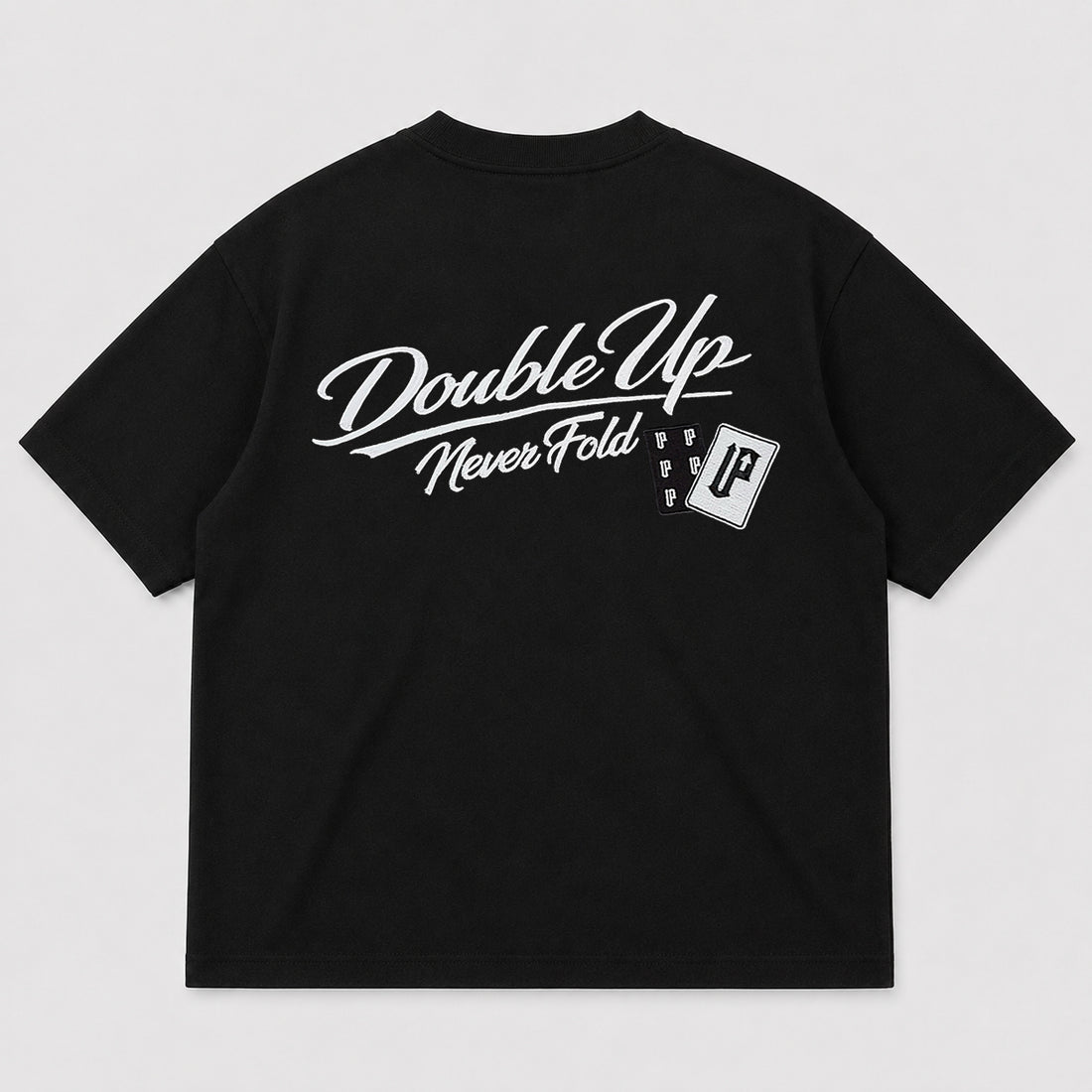 A black short-sleeve t-shirt shown from the back, featuring a white embroidered print that reads 'Double Up Never Fold' with a small vertical cards logo and a small rectangular patch graphic.