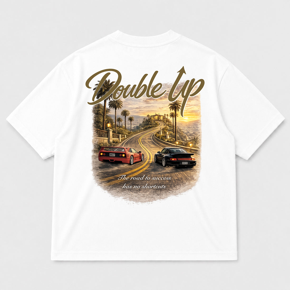 White short-sleeve t-shirt with a large graphic print on the back. The graphic features the words 'Double Up' in a metallic green script, above an illustration of a winding road with palm trees, a red sports car, a black sports car, and a sunset sky.