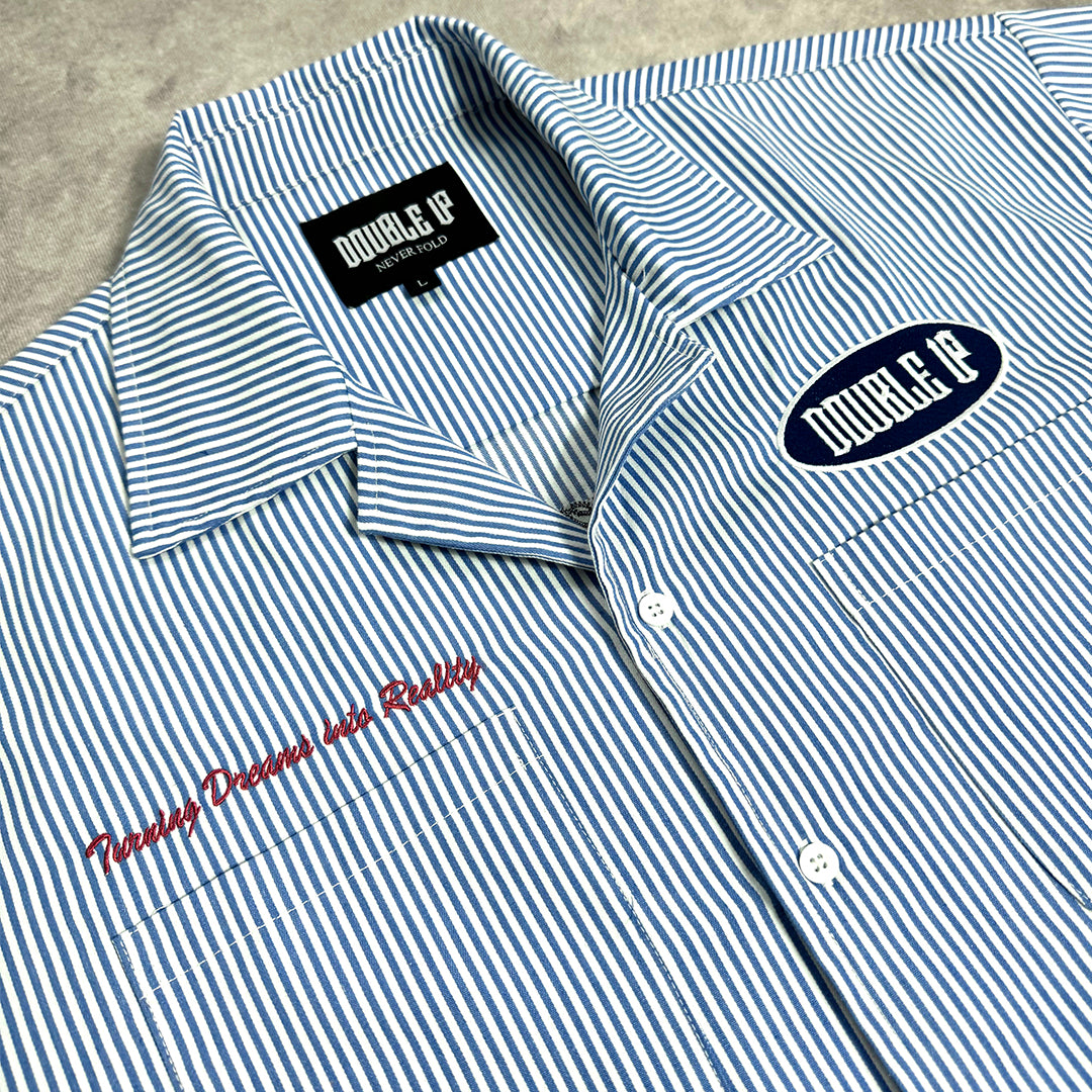 Blue and white striped shirt with embroidered text and logos on a gray surface