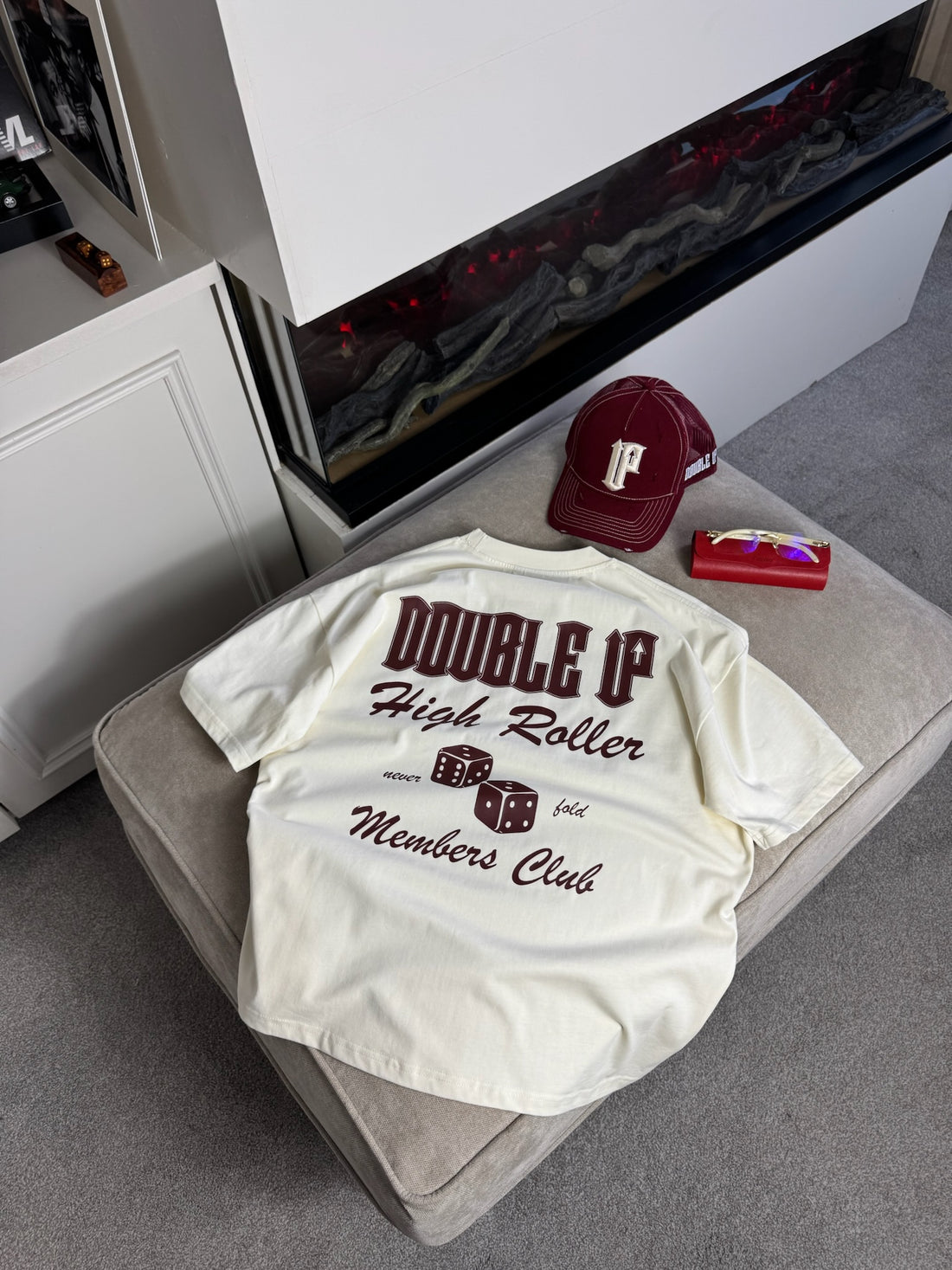 off white t-shirt with text and graphics on a chair next to a red cap and small box.