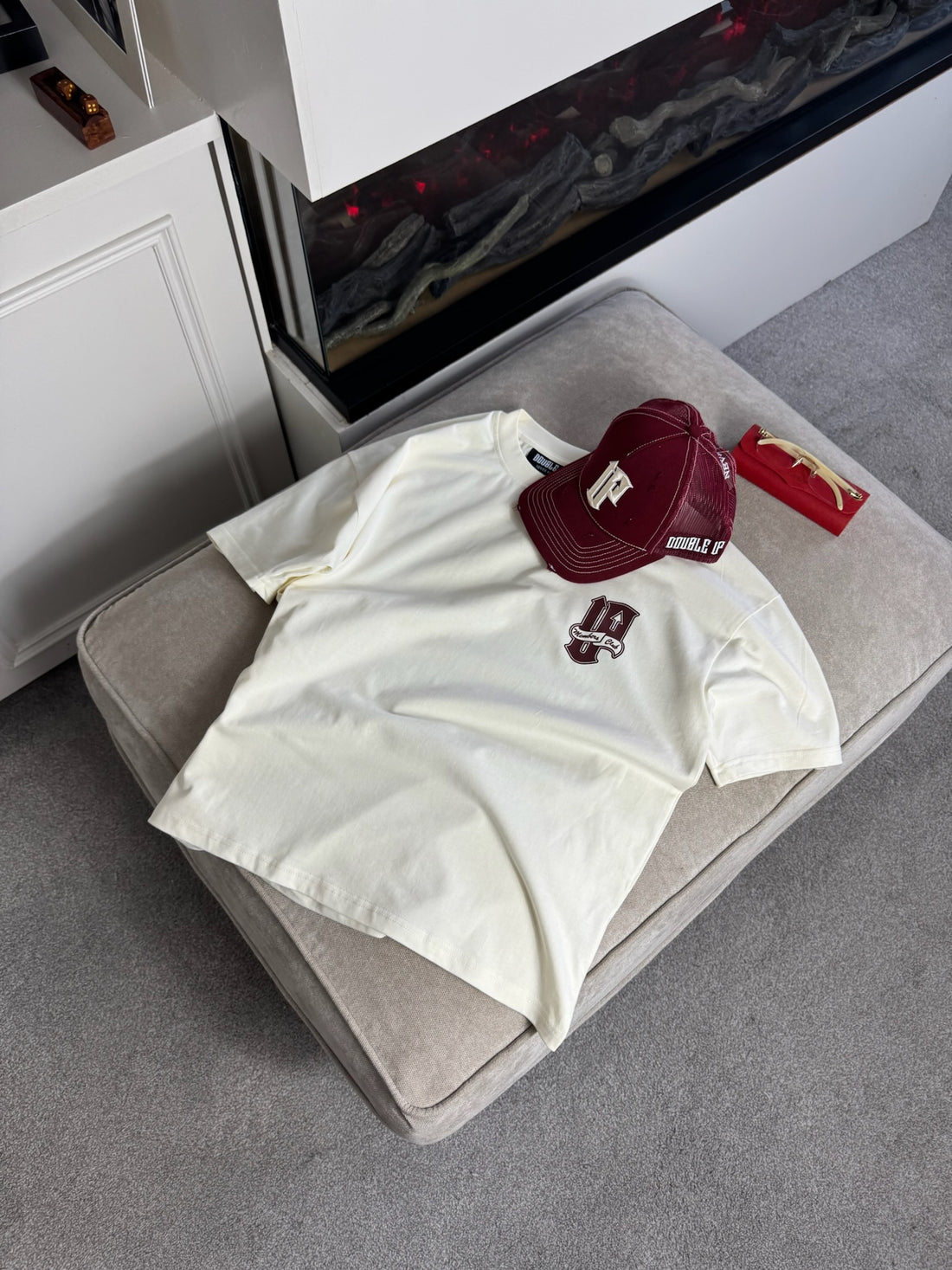 cream t-shirt with a red cap and small red box on a gray ottoman.