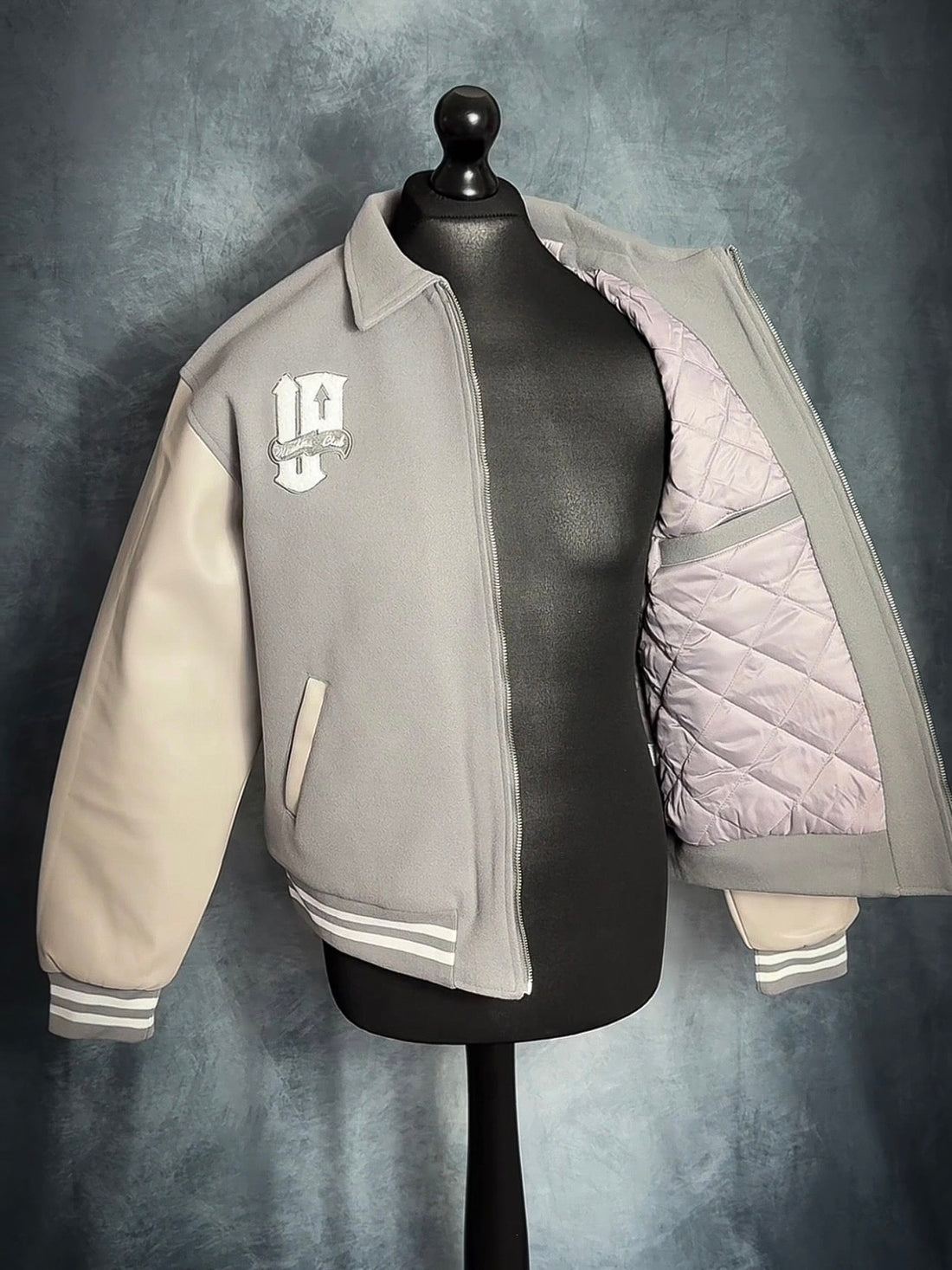 Gray and beige varsity jacket on a mannequin against a gray background